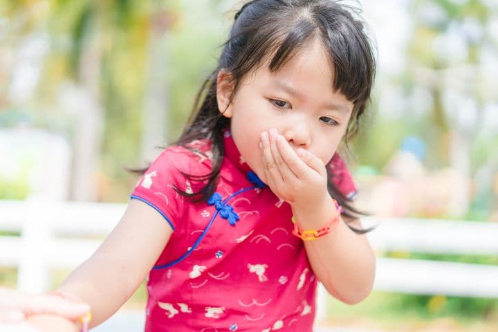 Little girl puts one hand over her mouth with a vomiting motion.