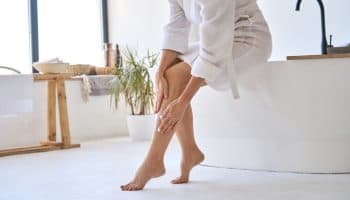 Woman touching her leg in a bathroom, showing that bullous cellulitis can start on the leg.