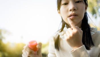 A girl touches her lip and applies ointment to heal a mouth ulcer.