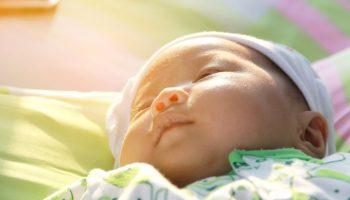 Close-up of an infant lying in bed with sunrays on her face.