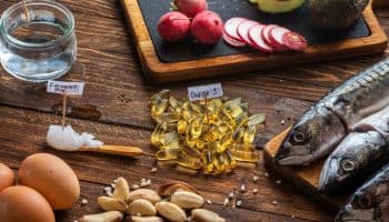 Foods containing different types of fat, such as eggs, brazil nuts, mackerel fish, and coconut oil, on a wooden table.