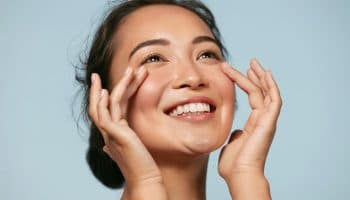 A woman smiling as she gently touches her cheeks with her forefingers.