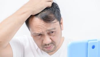 Middle-aged male looks at his hair in the mirror with a concerned expression.