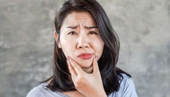 Woman with a concerned expression holds her chin, one side of her face slouching.