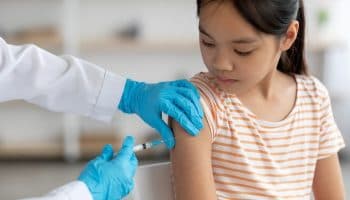 Young girl in her tweens is getting an injection to her shoulder administered by a health professional.