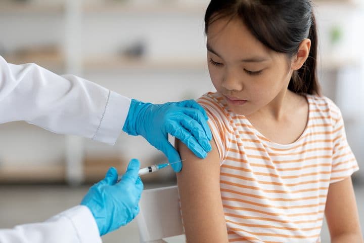 Young girl in her tweens is getting an injection to her shoulder administered by a health professional.