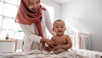 Baby boy sits up smiling while mother massages him gently.