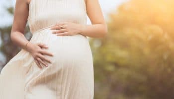 Pregnant woman with her hands on her belly and walking outdoors.