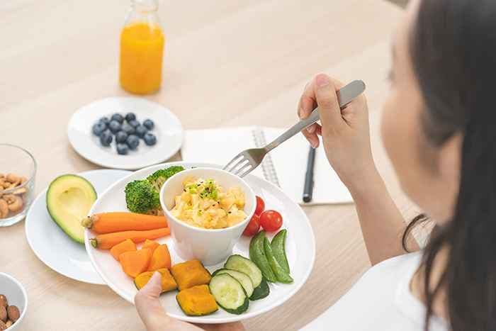 A woman holds a plate of vegetables with a small bowl of scrambled eggs.