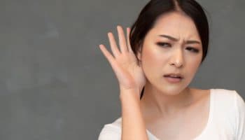 A woman holds a hand to her ear, indicating she is hard of hearing.