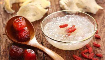 A spoon of red jujubes on the left and a bowl of bird’s nest on the right, set on a wooden table