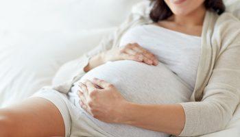 A pregnant woman holding her belly while sitting on a white bed