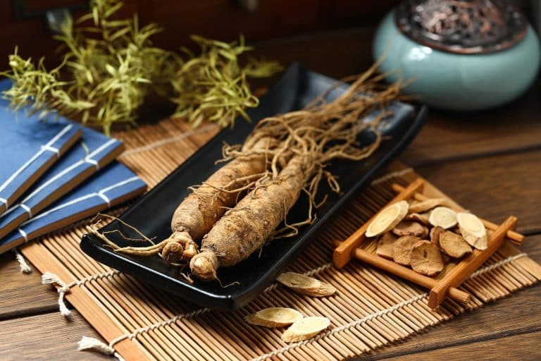 Two asian ginseng roots on a black modern plate placed on top of a bamboo mat