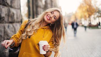 A beautiful white woman smiling in the city holding a cup of coffee