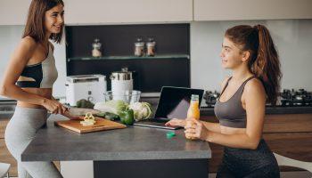 Two women wearing gym clothes preparing meals in the kitchen