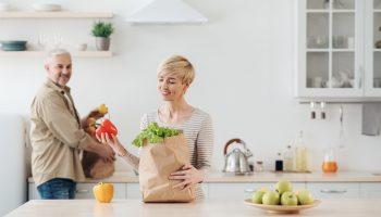 a young woman and a senior man unloading groceries filled with anti aging foods in the kitchen