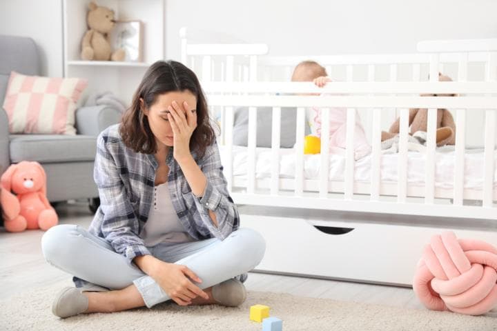 A woman feeling sad after giving birth, baby on the crib