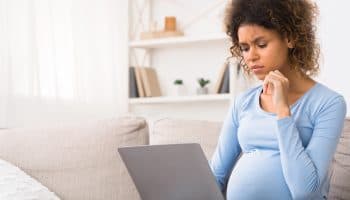 A pregnant woman sitting on a sofa looking at her laptop