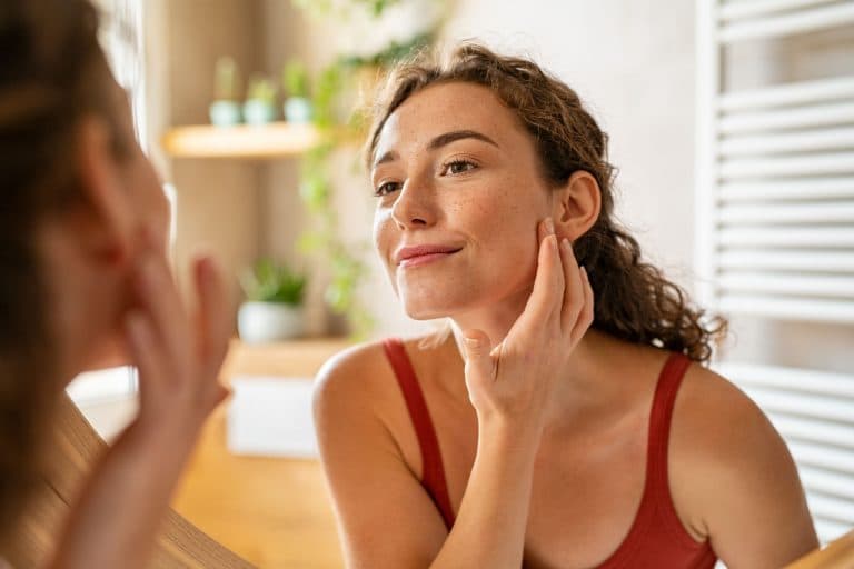 A young beautiful woman with freckle skin checking her skin conditions in a mirror