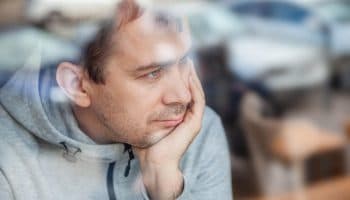 A somber man is showing depression symptoms while looking out the window