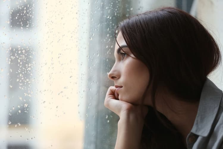 A depressed young woman looking out the window into the rain