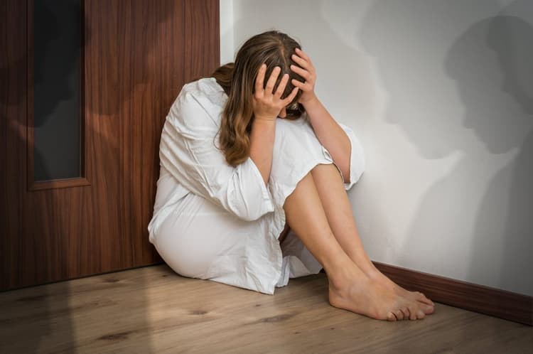 A hallucinating woman sitting in the corner of the room with her head in her hands as shadows appear on the wall