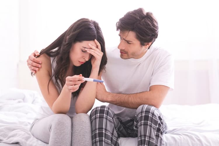 A young woman holding a negative pregnancy test experiencing infertility being comforted by her partner